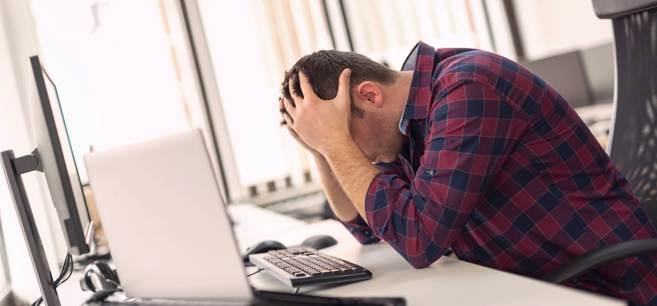 Man sitting at desk with hands placed on head